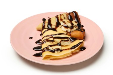 Beyaz arka planda çikolata soslu ve muz dilimli krep tabağı.