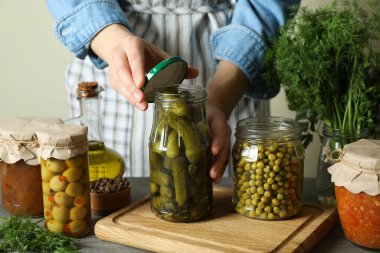 Kadın bir kavanoz salatalık turşusunu ahşap arka planda turşulu yiyecekle kapatır.