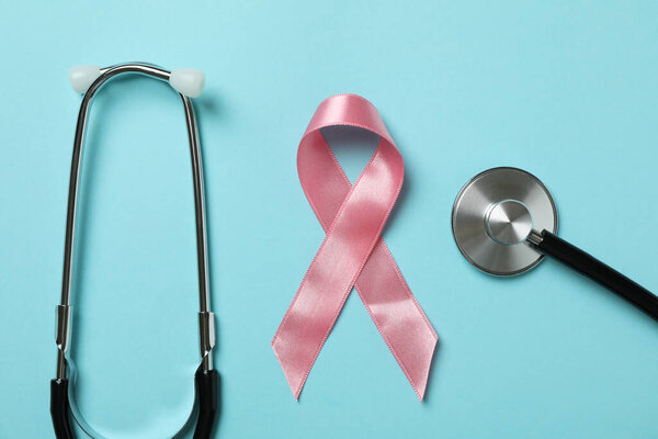 Pink awareness ribbon and stethoscope on blue background