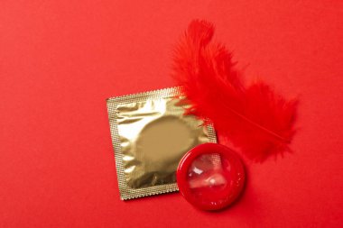 Kırmızı arka planda prezervatif ve kırmızı tüy.
