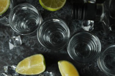 Bir şişe votka, shot, buz küpleri ve siyah dumanlı masada limon dilimleri.