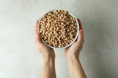 Beyaz desenli arka planda bir kase nohut tutan kadın elleri.