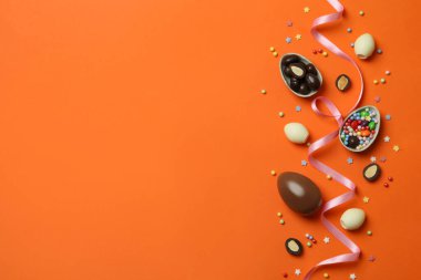 Paskalya çikolatası yumurtaları, şekerler ve turuncu arka planda serpiştirmeler