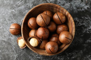 Siyah dumanlı arka planda lezzetli macadamia fındıkları olan kase.