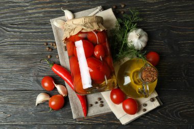 Kavanoz dolusu domates ve malzemeler ahşap masada.