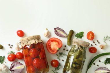 Kavanozlar dolusu salatalık, domates ve beyaz arka plandaki malzemeler.