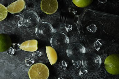 Bir şişe votka, shot, buz küpleri ve siyah dumanlı masada limon dilimleri.