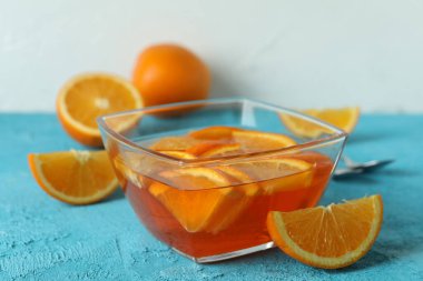 Mavi desenli arka planda portakal dilimleri olan bir kase turuncu jöle.