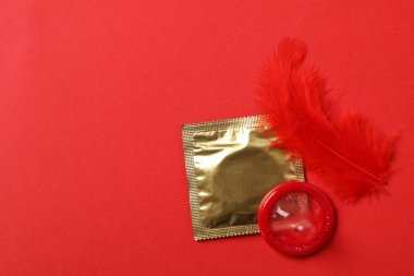 Kırmızı arkaplanda prezervatif ve tüy, metin için boşluk