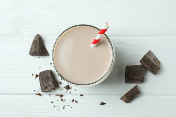 Glass of chocolate milkshake and chocolate pieces on white wooden table