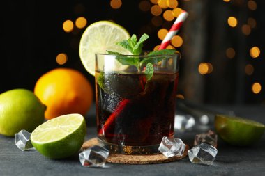 Bulanık ışıklara karşı gri desenli masada Küba Libre bardağı