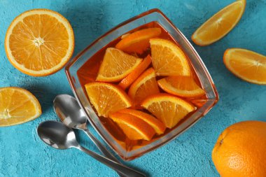 Mavi desenli arka planda portakal dilimleri olan bir kase turuncu jöle.