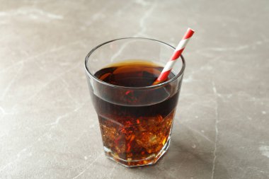 Buzlu bir bardak kola ve gri masada saman.