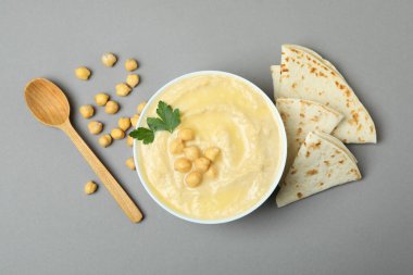 Gri arka planda bir kase humus, pide ve kaşık.