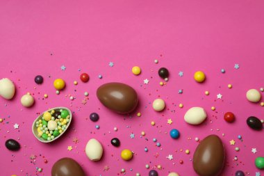 Paskalya çikolatası yumurtaları, şekerler ve pembe arka planda serpiştirmeler