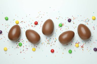 Paskalya çikolatası yumurtaları, şekerler ve beyaz arka plana serpiştirilmiş şekerler.