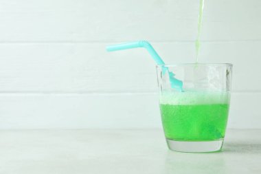 Soda beyaz ahşap arka planda bir bardağa dökülüyor.