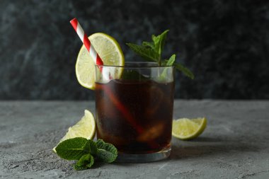 Bir bardak Küba Libre ve gri masadaki malzemeler.