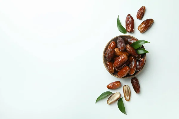 Bowl of dried dates with leaves on white background