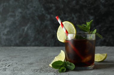 Bir bardak Küba Libre ve gri masadaki malzemeler.