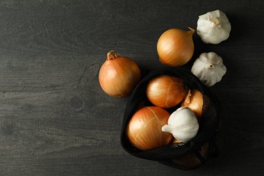 Siyah ahşap masada soğanlı ve sarımsaklı çanta.