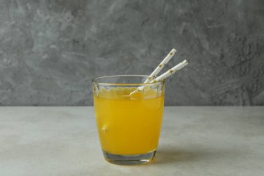 Beyaz desenli masada gri arka planda bir bardak portakallı soda.