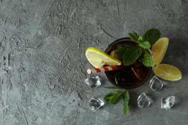 Bir bardak Küba Libre ve gri masadaki malzemeler.