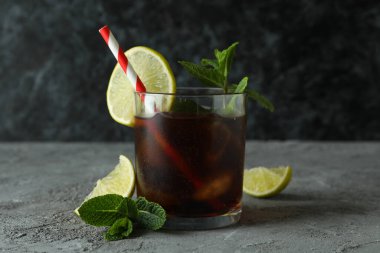 Bir bardak Küba Libre ve gri masadaki malzemeler.