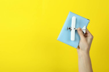 Kadın el ele tutuşan oyuncak uçak ve sarı arka planda pasaport