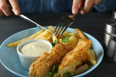 Koyu masada kızarmış balık ve patates yiyen bir kadın.