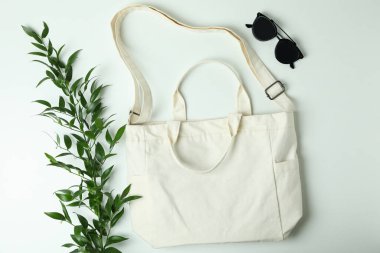 Beyaz arkaplanda boş tekstil çantası, dal ve güneş gözlüğü