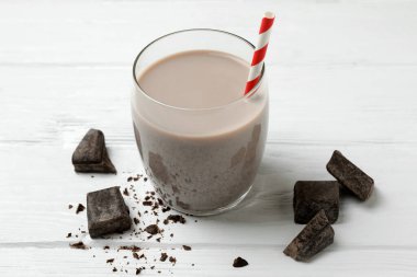 Bir bardak çikolatalı milkshake ve beyaz ahşap masada çikolata parçaları.