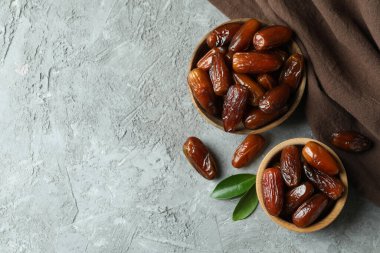 Bir kase kuru hurma ve gri desenli arka planda mutfak peçetesi.