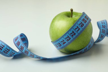 Beyaz zemin üzerinde mezura olan yeşil elma