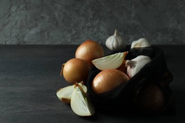 Siyah ahşap masada soğanlı ve sarımsaklı çanta.