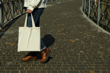 Genç bir kadın açık havada boş bir eco çantası tutuyor.