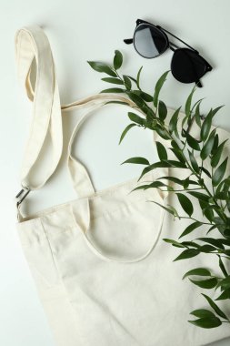 Beyaz arkaplanda boş tekstil çantası, dal ve güneş gözlüğü