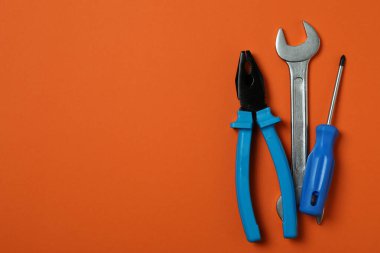 Turuncu arka planda tornavida, anahtar ve kerpeten.