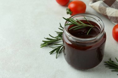 Barbekü sosu kavanozu, biberiye, domates ve mutfak havlusu beyaz desenli masa.