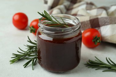 Barbekü sosu kavanozu, biberiye, domates ve mutfak havlusu beyaz desenli masa.