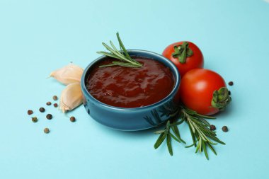 Bir kase barbekü sosu ve mavi arka planda baharatlar.