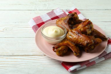 Fırında tavuk kanatlı tabak ve ahşap arka planda mutfak havlusuna sos.