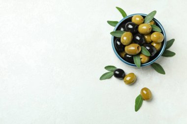 Beyaz desenli arka planda bir kase zeytin ve yapraklar