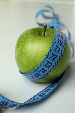 Beyaz zemin üzerinde mezura olan yeşil elma