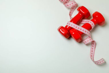Beyaz arkaplanda kırmızı halterler ve mezura.