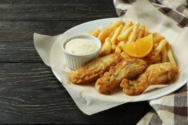 Mutfak havlusuyla ahşap zemin üzerinde kızarmış balık ve patates kızartması tabağı