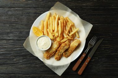 Ahşap arka planda lezzetli kızarmış balık ve patates kızartması tabağı.