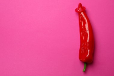 Pembe arka planda kırmızı prezervatifli kırmızı biber.