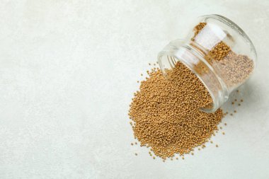 Beyaz desenli arkaplanda hardal tohumları olan cam kavanoz.