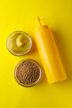 Sarı zemin üzerinde hardal ve sos şişesi olan kaseler.